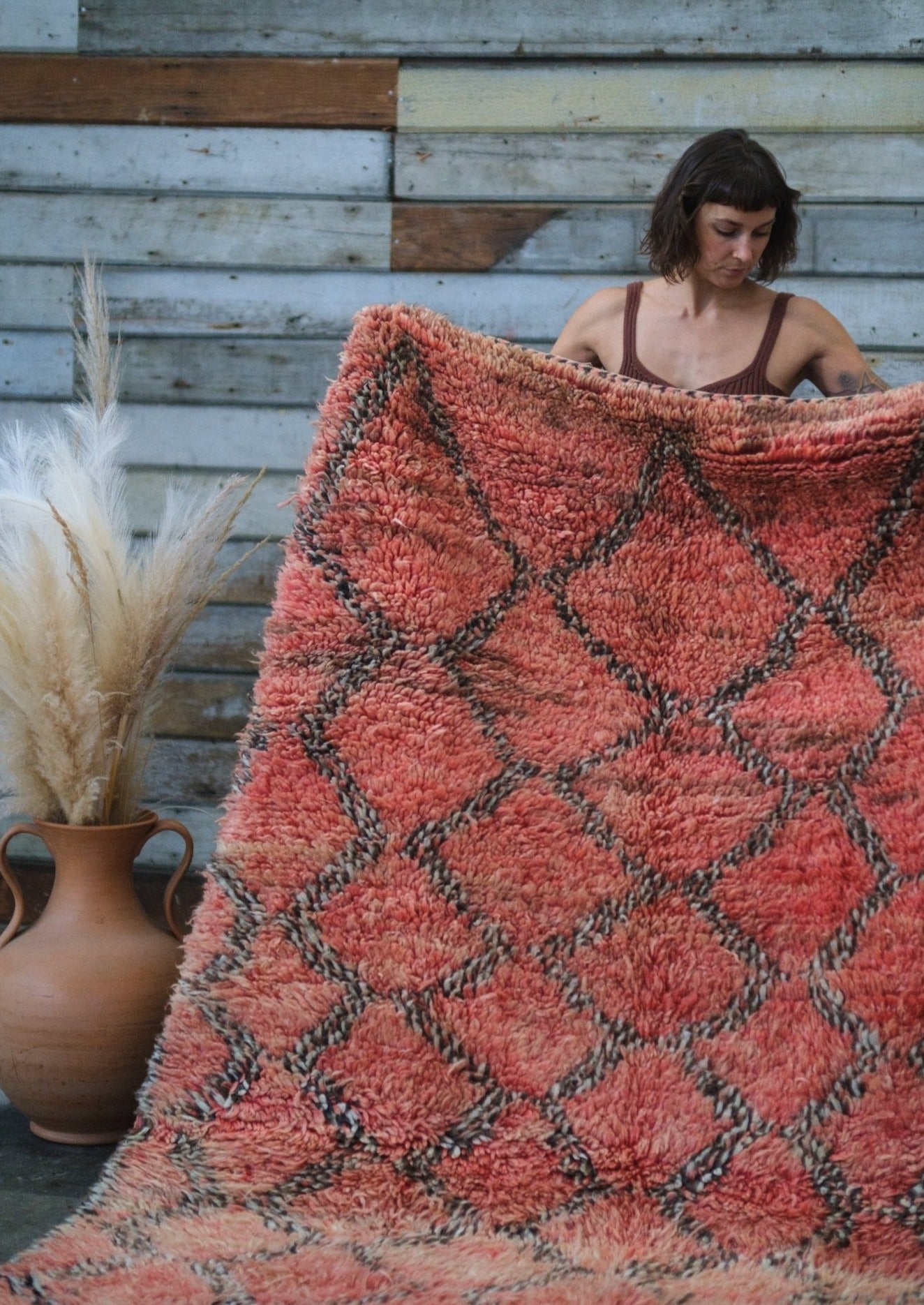 girl holds moroccan rug lovingly as she examines the hand woven qualities. rug is a soft red with specked black diamonds woven into the wool.