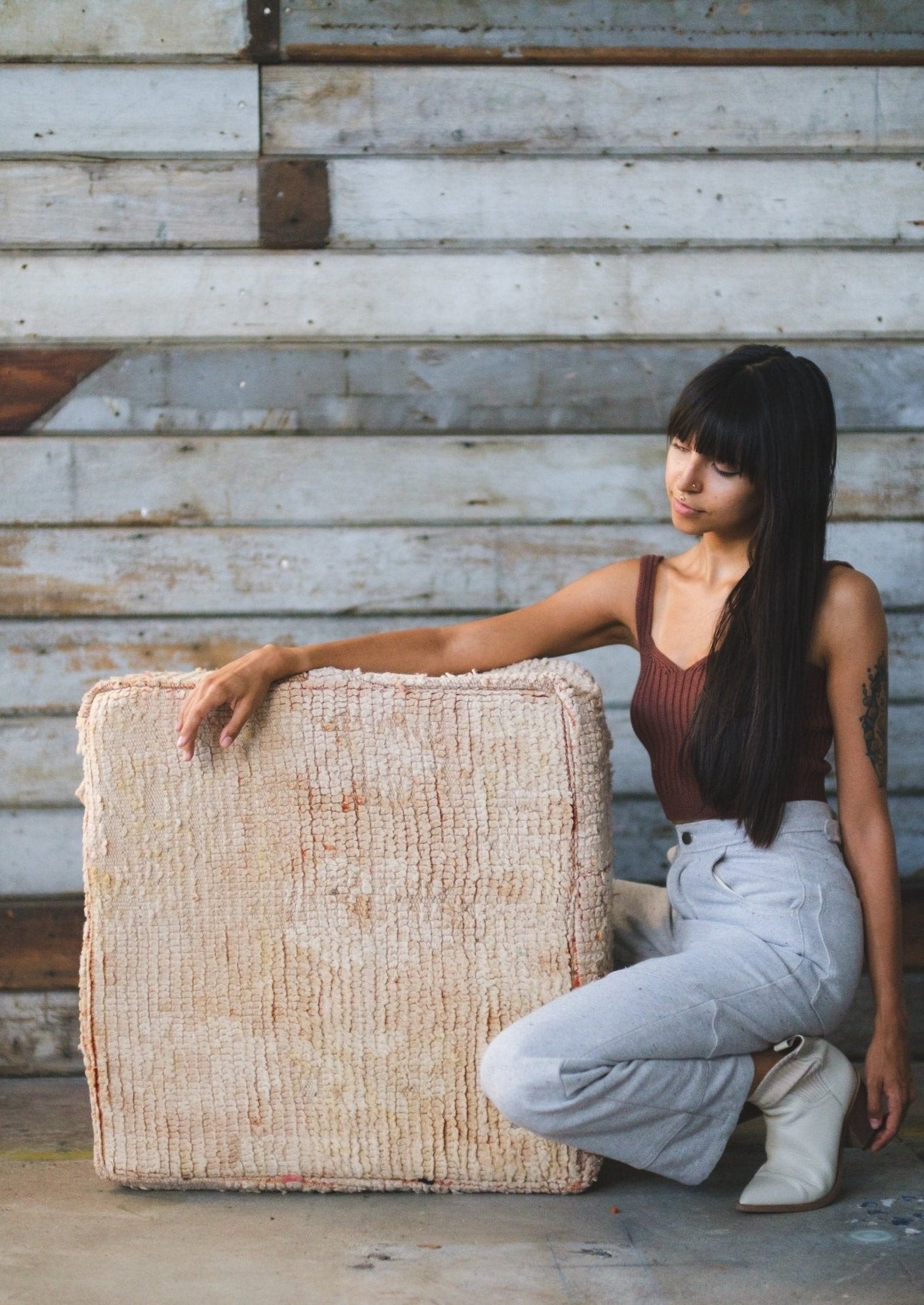 washed out moroccan floor cushion sitting on ground with cute girl resting her arm on it with long dark hair and bangs. she is wearing soluna collective made from organic fibers. 
