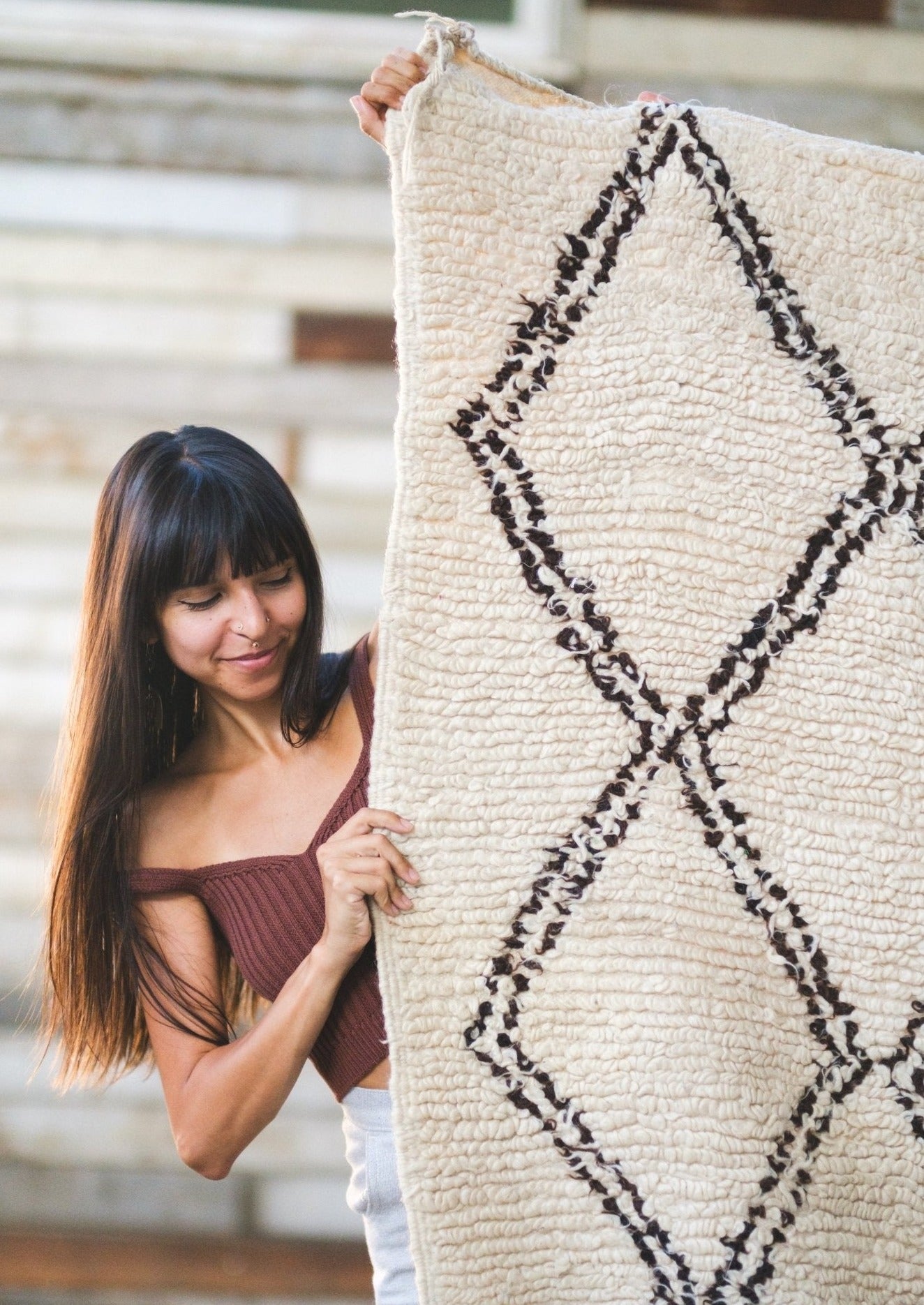 cute girl peeks around beni ourain rug wearing soluna collective top made from organic fibers. rug is made of 100% white wool with black diamonds.