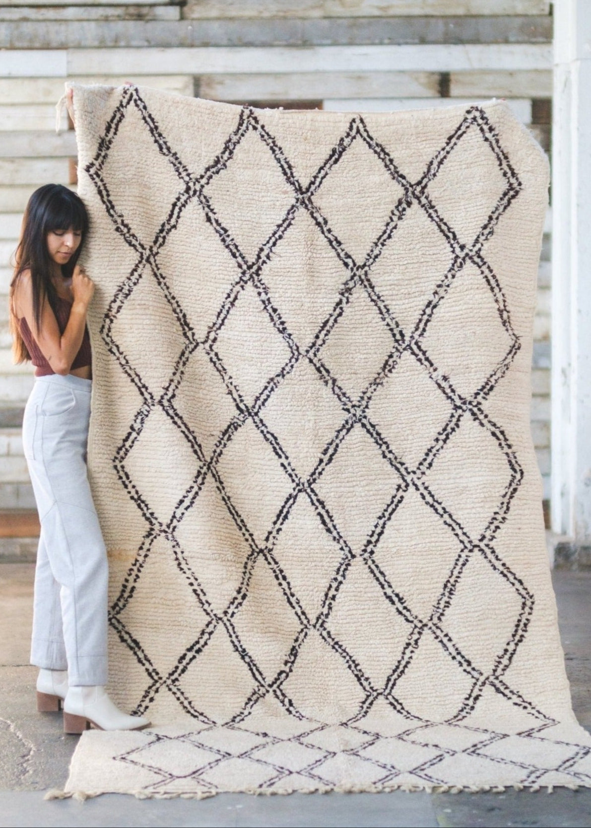 girl holds classic beni ourain rug close, lovingly adores it and is cozy soft standing in rustic scene
