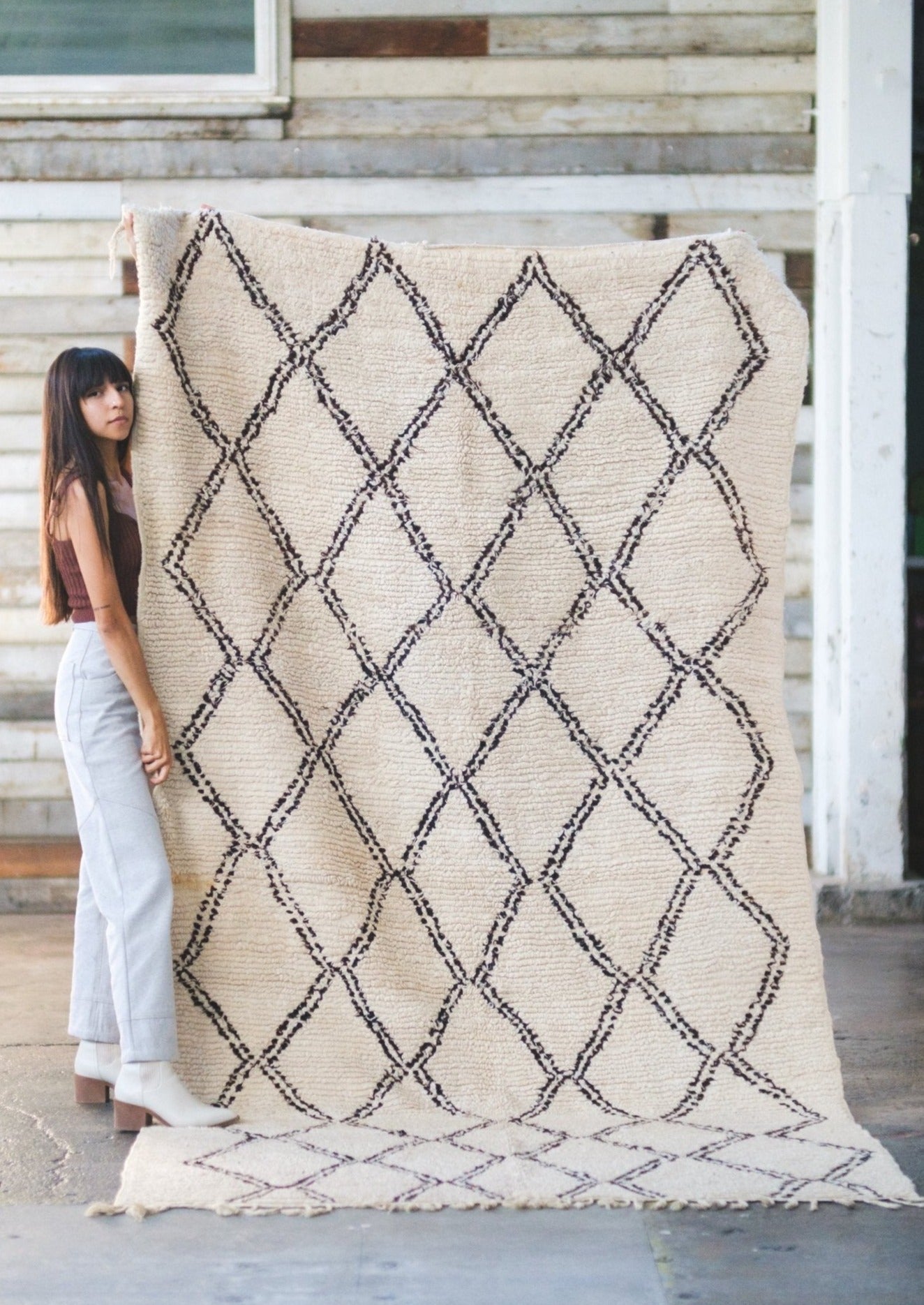 girl looks directly at you with a serious tone. she is young and honest with her ethos while lovingly holding a classic beni ourain moroccan rug