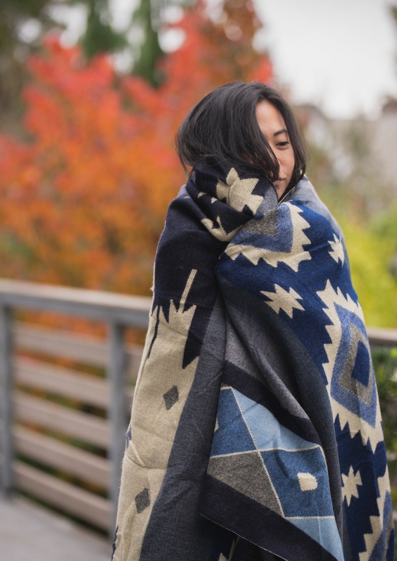asian girl takes a walk in the fall over a wooden bridge wrapping up in an alpaca blanket thats blue.