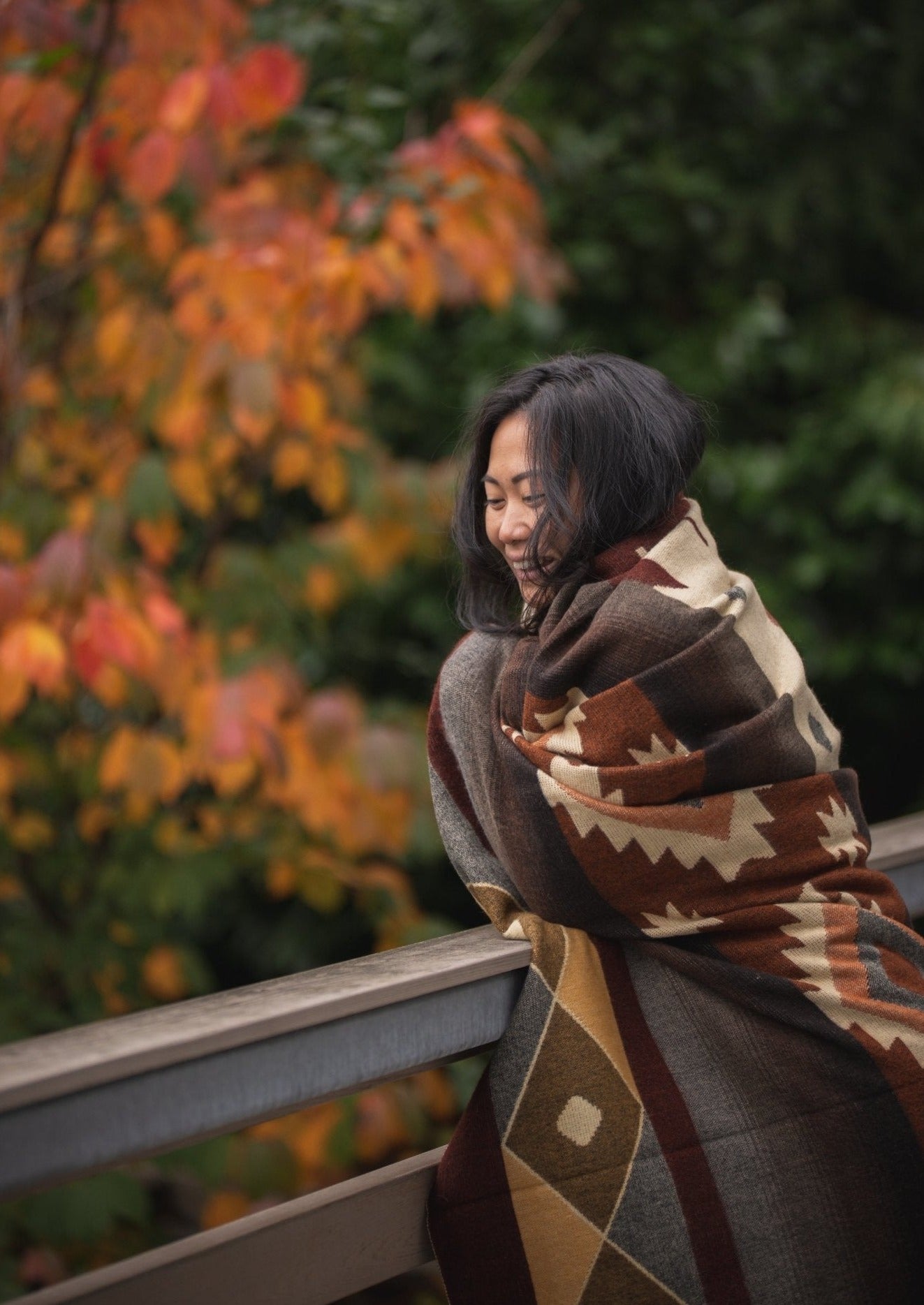 Asian girl goes for a walk in the Fall wrapped up in her soft alpaca blanket woven in Ecuador. She is smiling and happy.