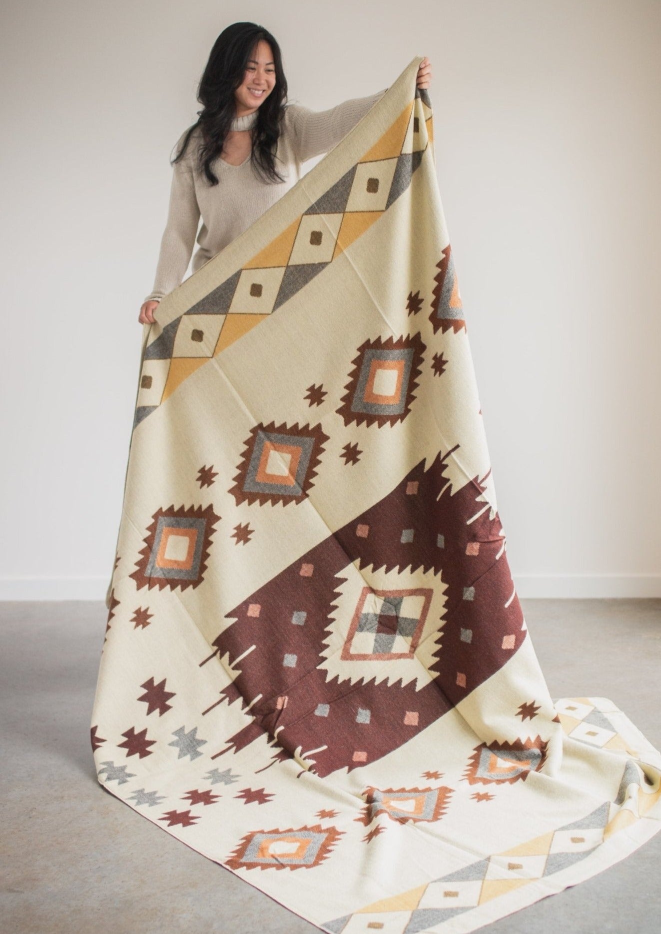 Asian girl wearing cozy sweatshirt holds up reverse side of alpaca blanket to show off the design.