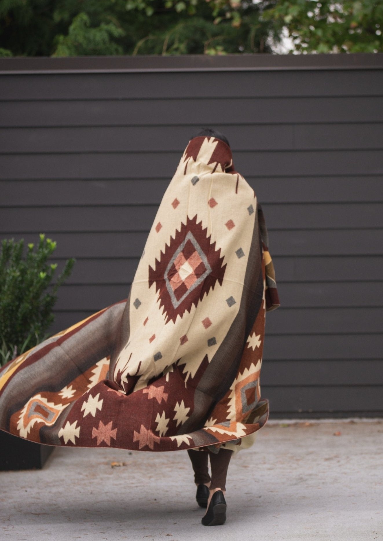 girl walks outside with brown alpaca blanket wrapped around her while the wind blows 