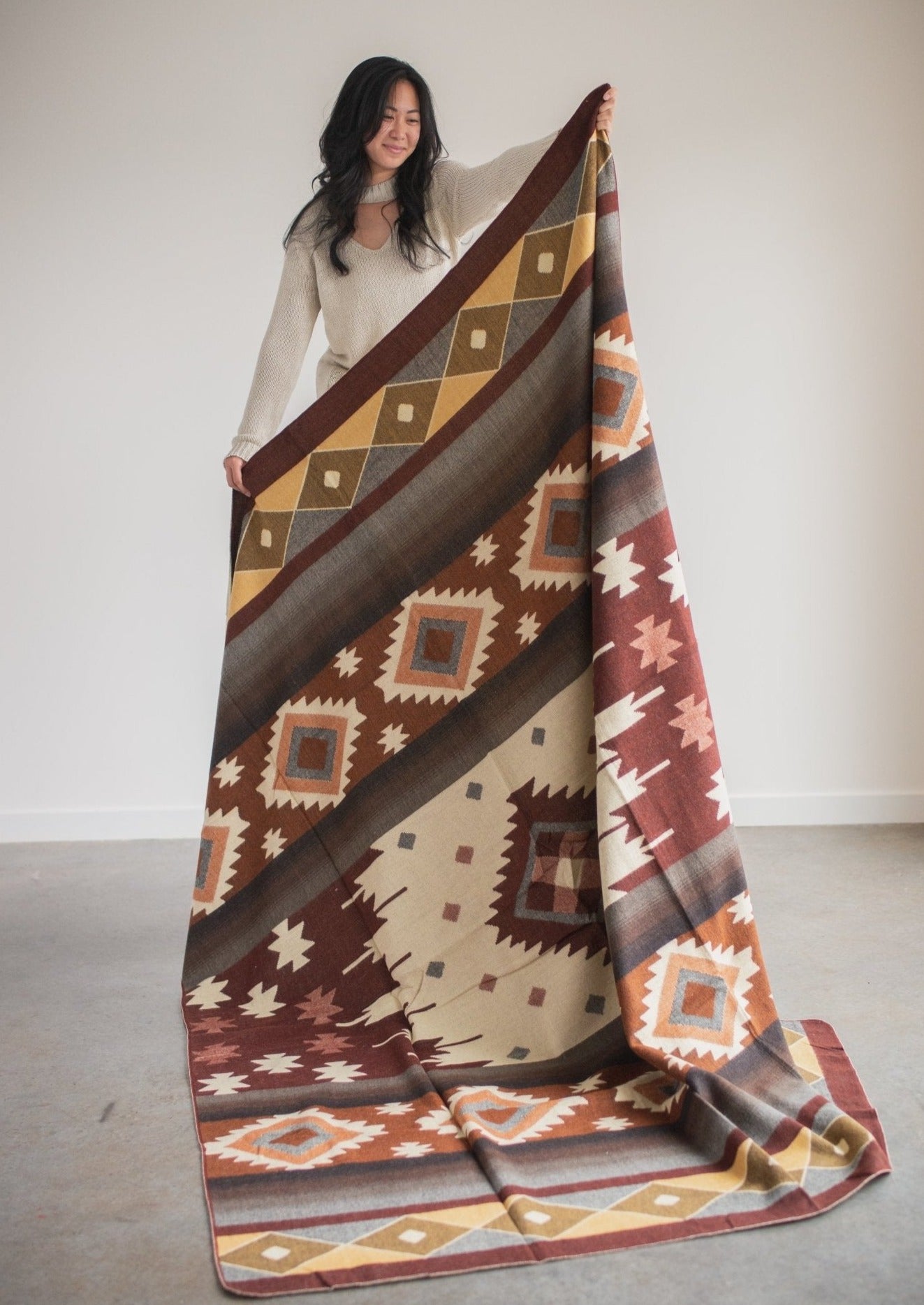 asian girl wearing cozy sweater holds up an alpaca blanket to show off the full design.