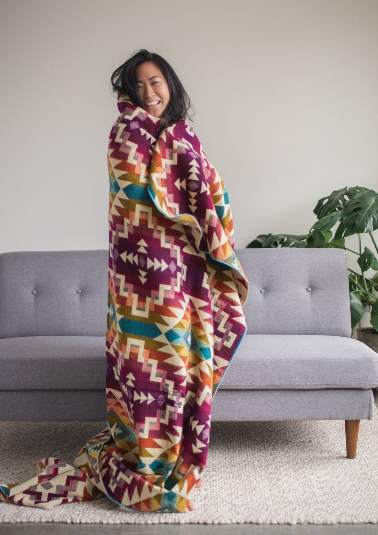 Asian girl is glowing with happiness standing in her living room wrapped in a soft alpaca blanket