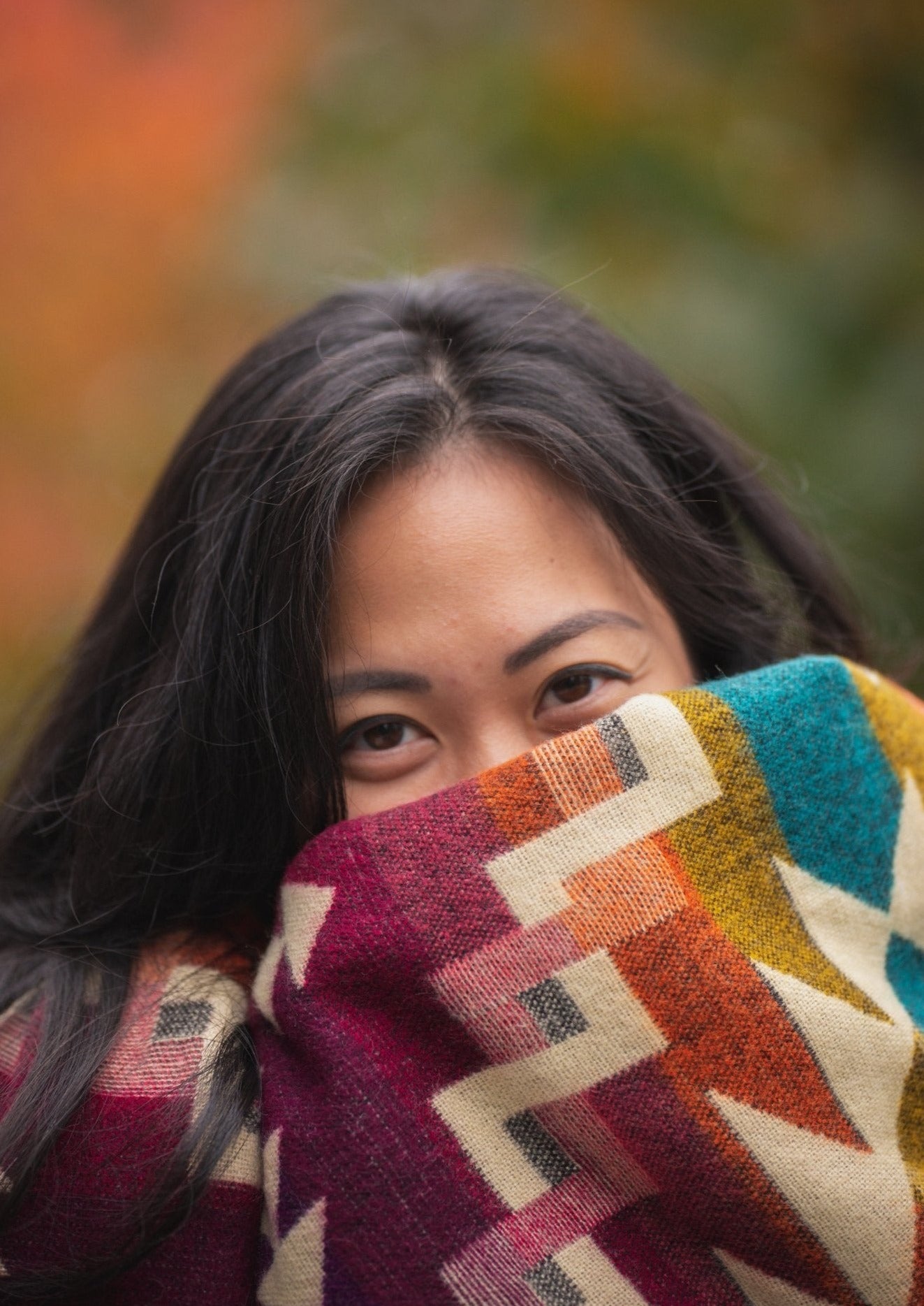 Asian girl cozies up in an alpaca blanket while taking a walk to see the the Fall colors.