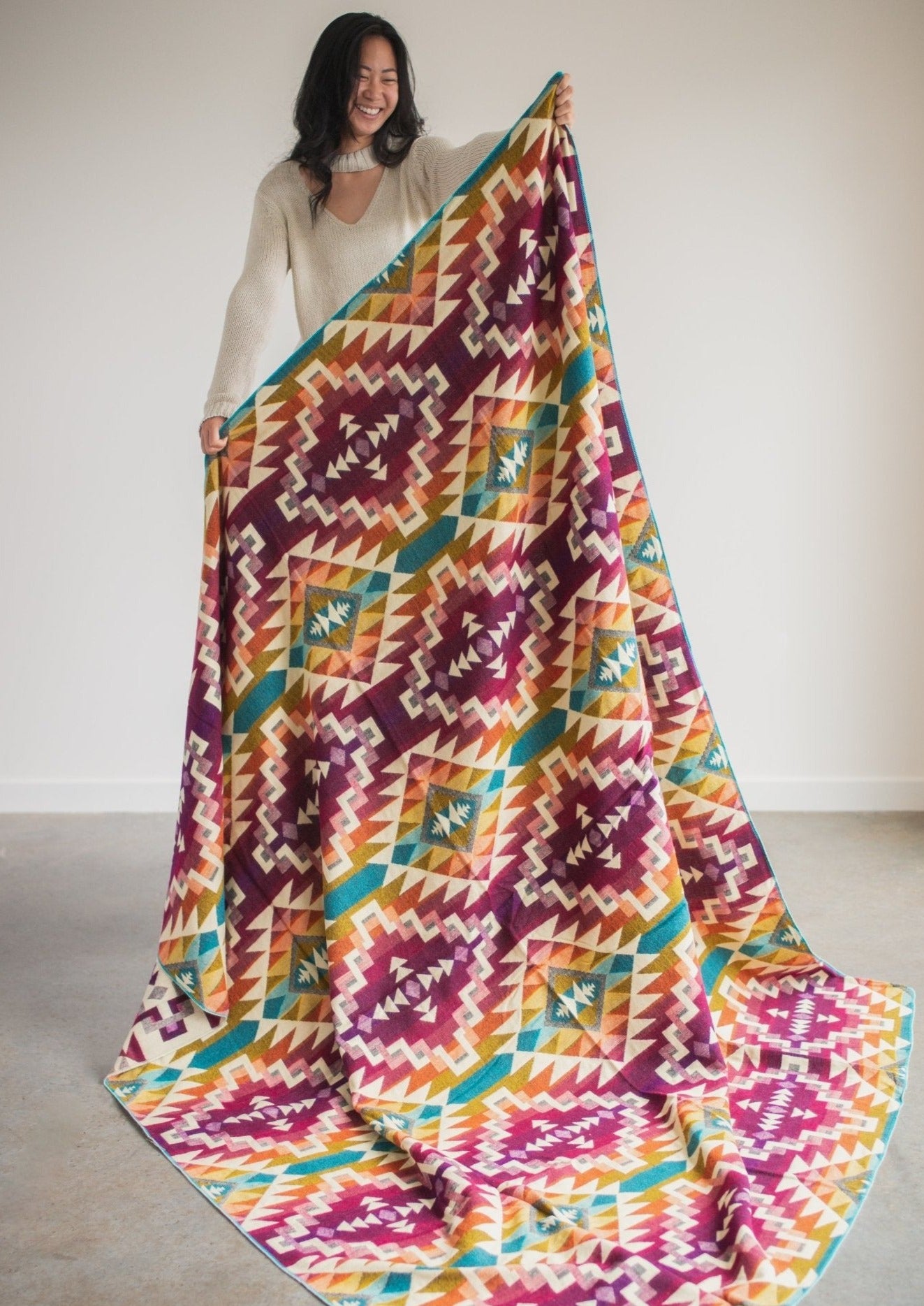 Asian girl wearing cozy sweater holds up alpaca blanket to see full design