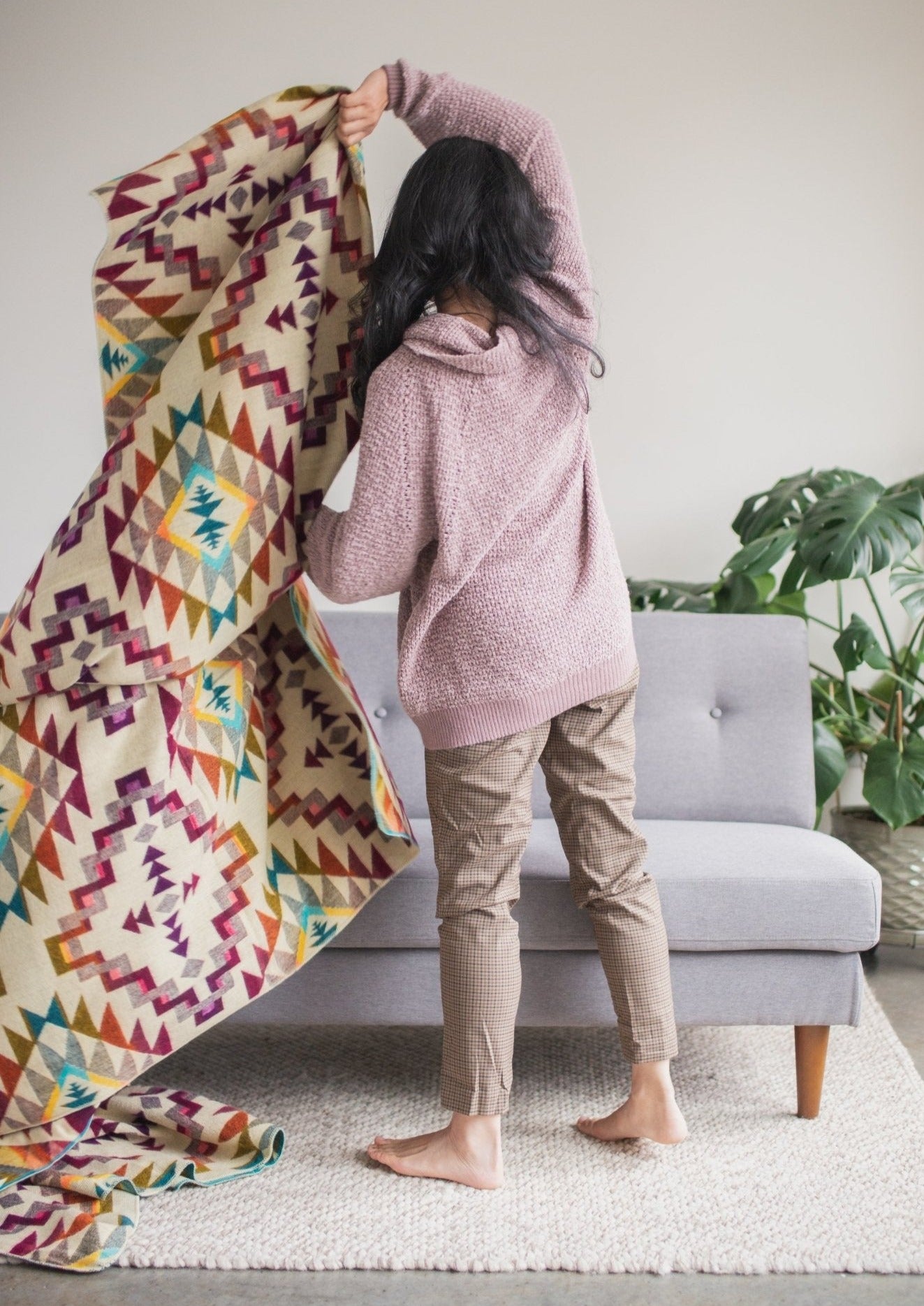 Asian girl is standing in her living room wearing comfy clothes on a sunday. she is in motion about to wrap her self up to get cozy. she shows off reverse side of alpaca blanket