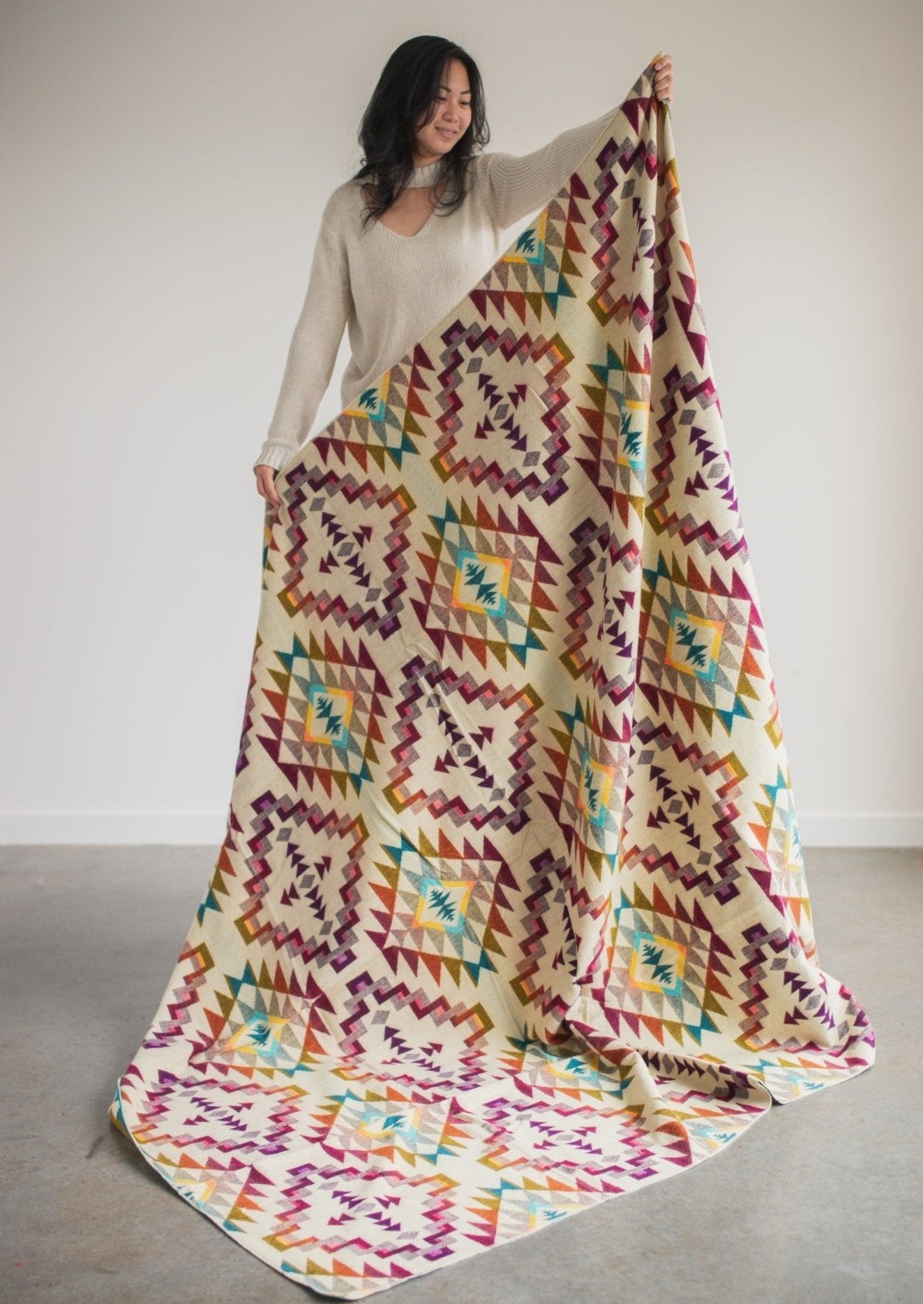 Asian girl wearing cozy sweatshirt holds up reverse side of alpaca blanket to show off full design.