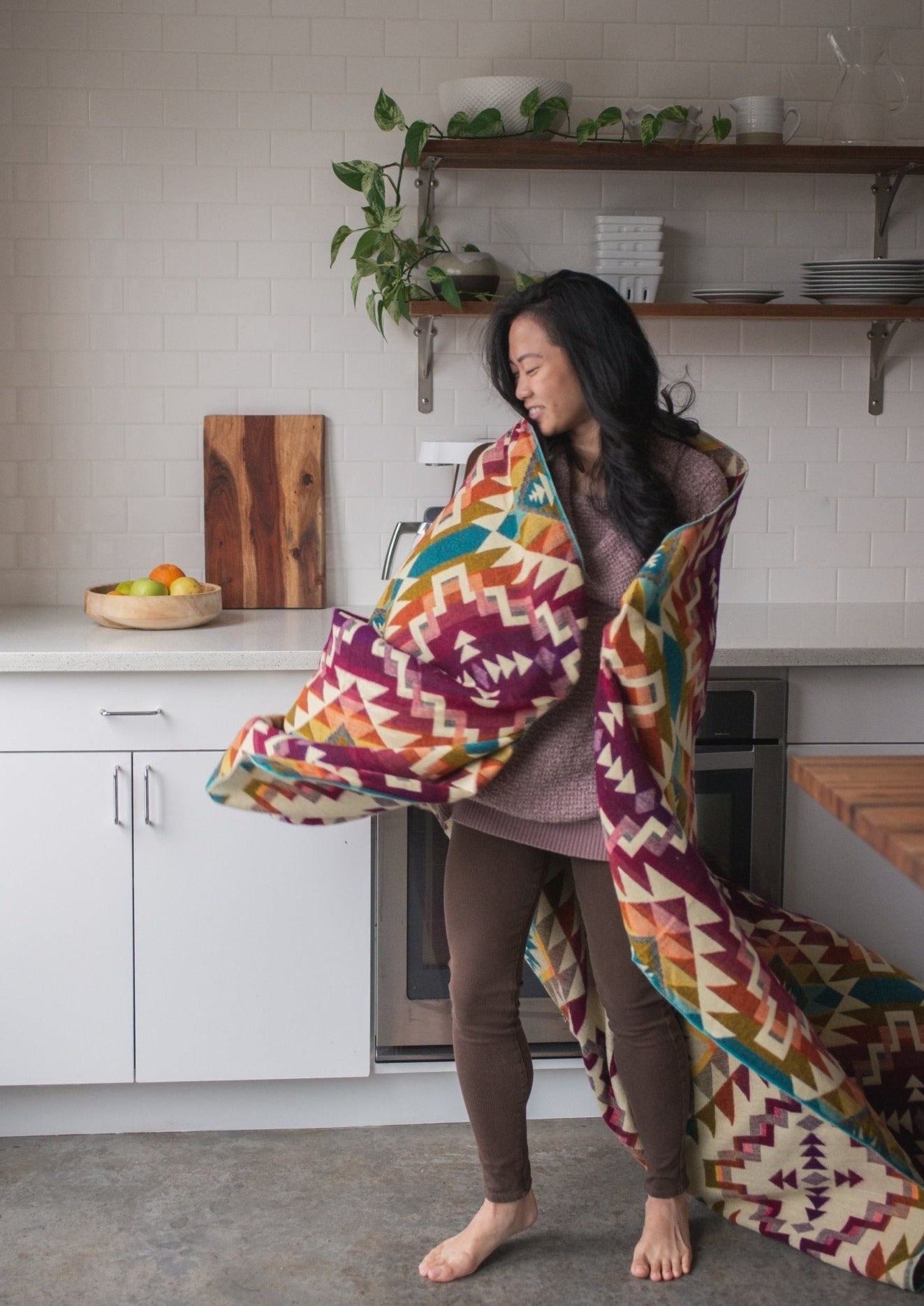 Asian girl dances in her modern kitchen with pure happiness with her cozy alpaca blanket woven in pinks. 