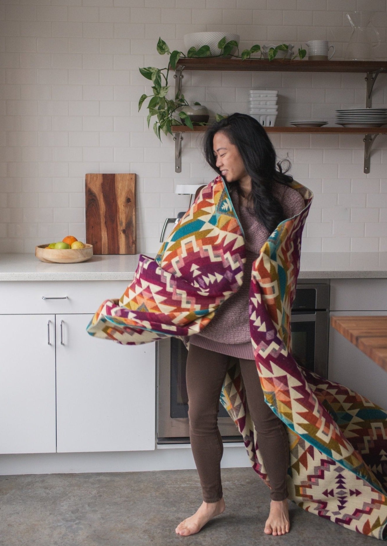 Asian girl dances in her modern kitchen with pure happiness with her cozy alpaca blanket woven in pinks.