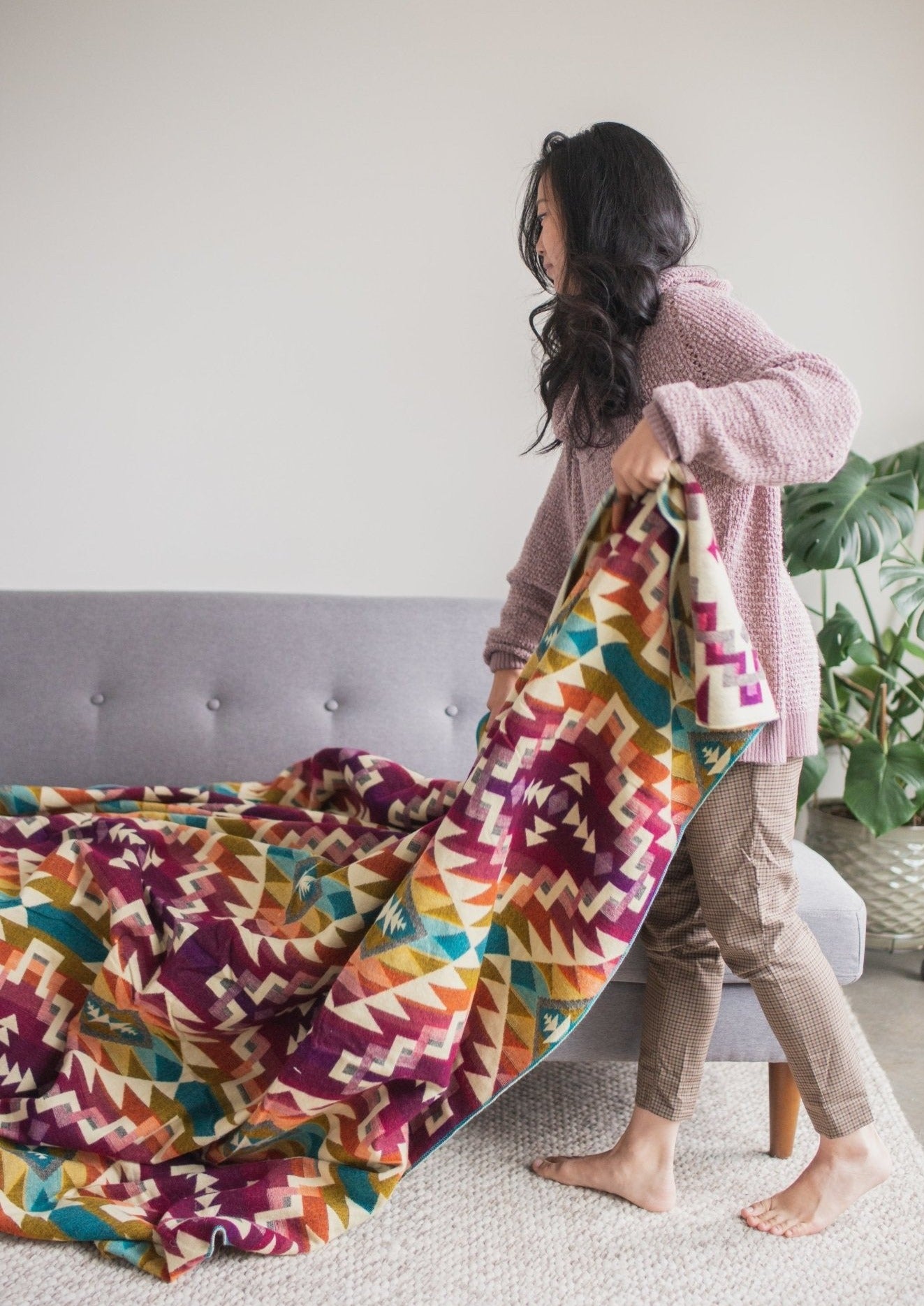 Asian girl wearing comfy clothes in her living room folds up her alpaca blanket after an afternoon lounging at home