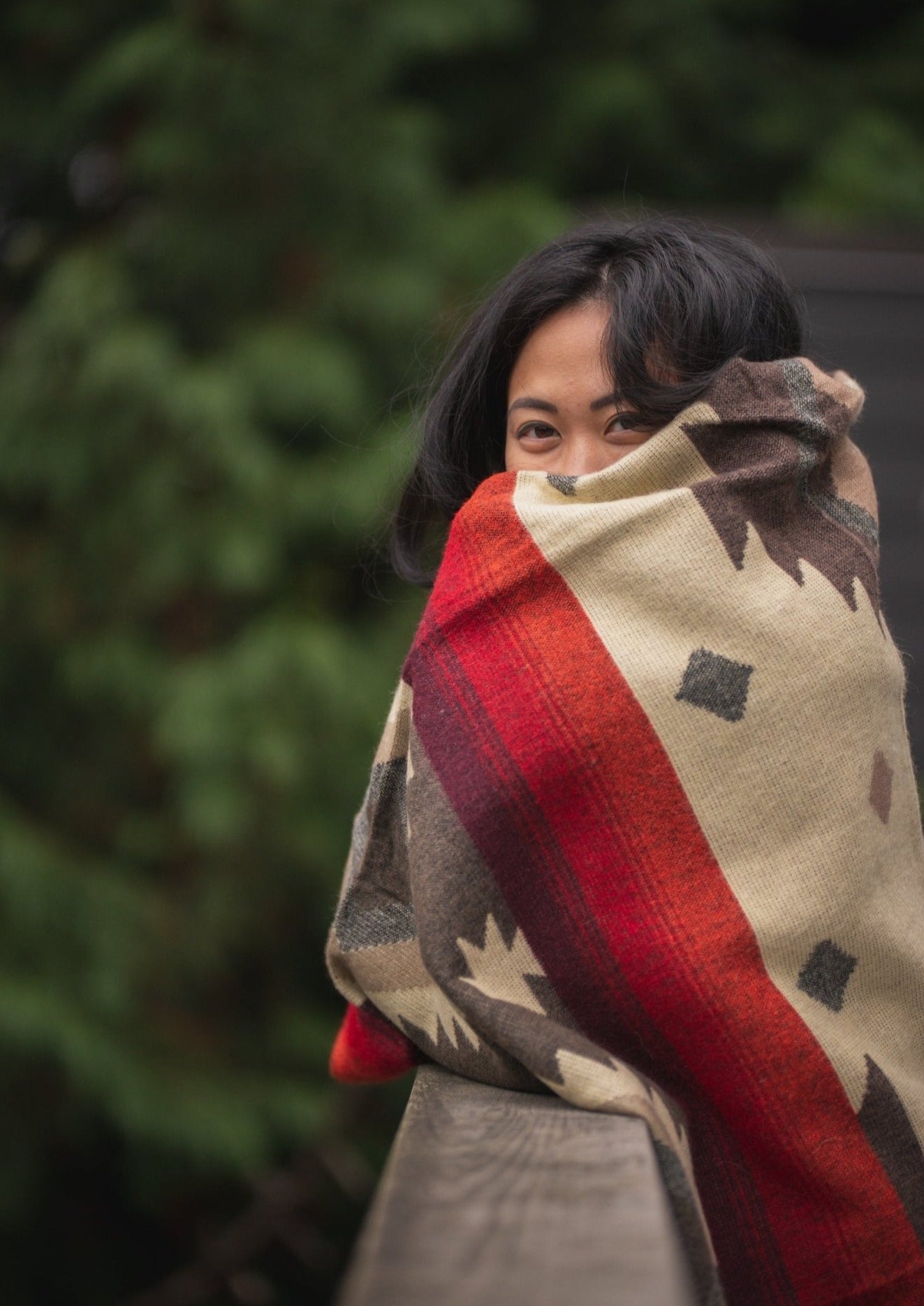 Asian girl goes for a walk outside with her cozy alpaca blanket. She gazes at the green forest while standing on a bridge. 