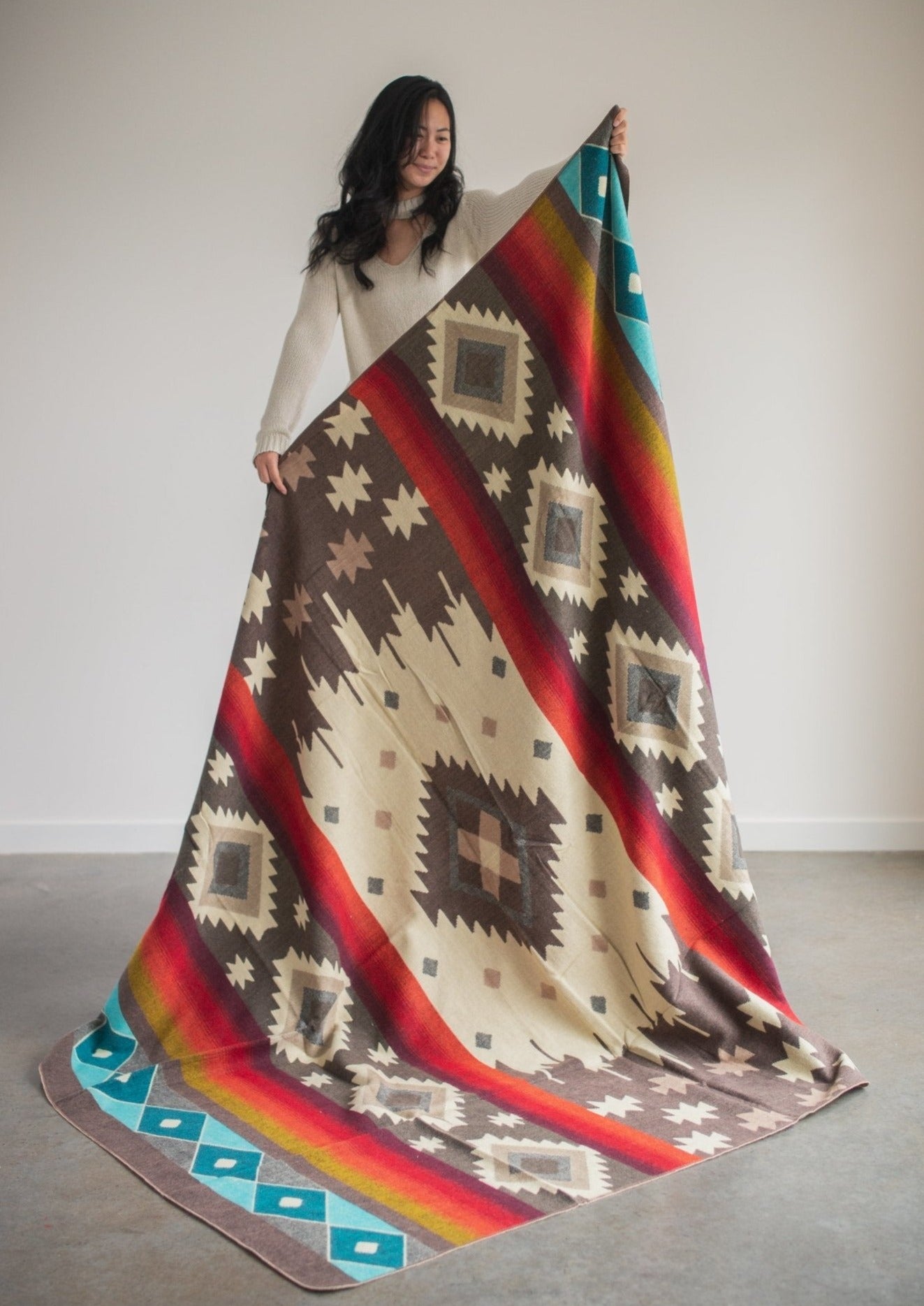 Asian girl wearing a cozy sweater holds up a red alpaca blanket to display full design
