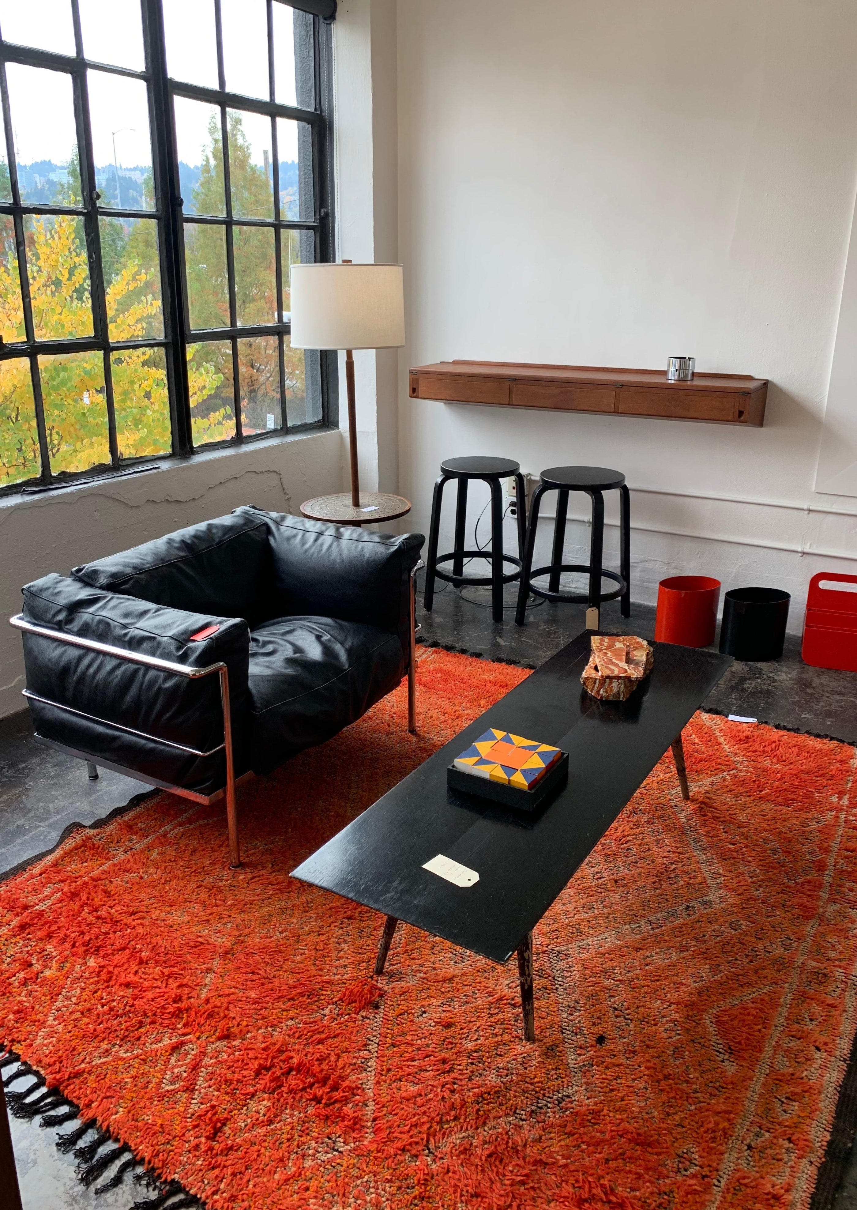 red rug in contemporary modern apartment with leather black chair black coffee table and cement floors with large windows 