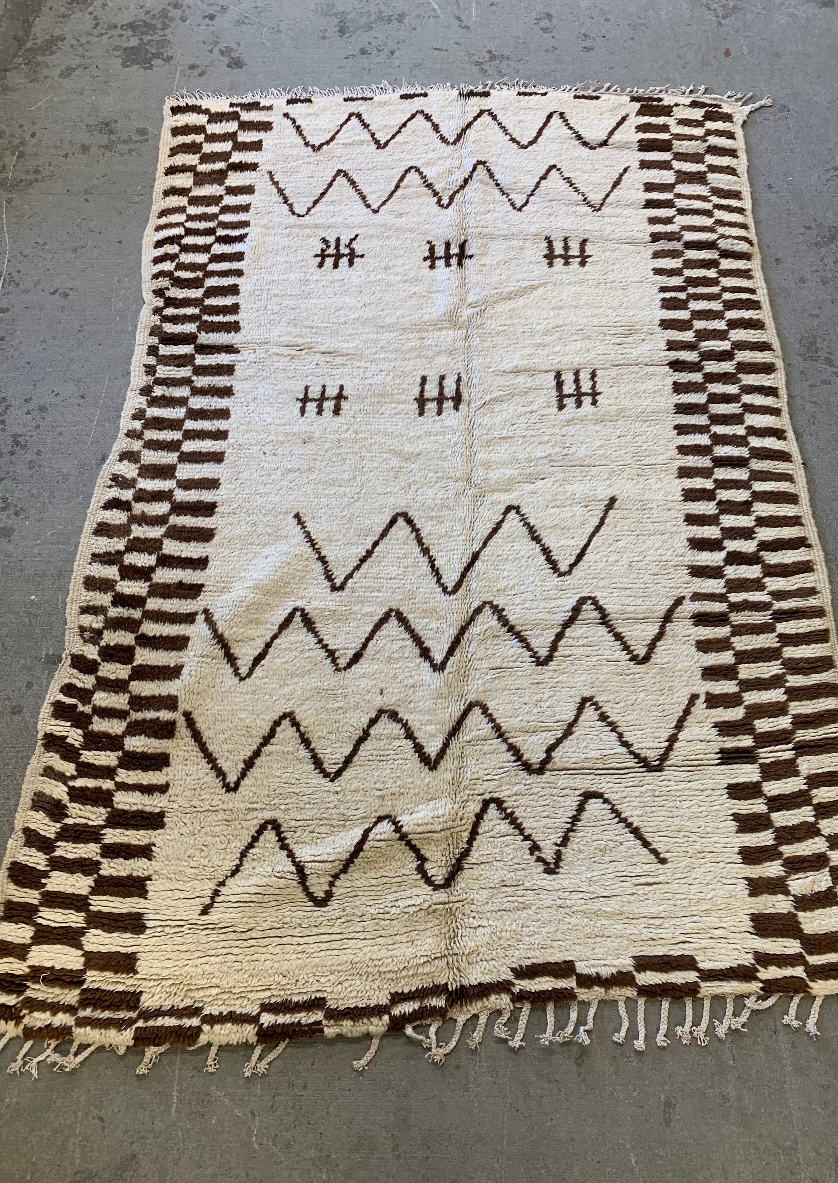 brown and white checkered rug with berber geometric designs on cement floor 
