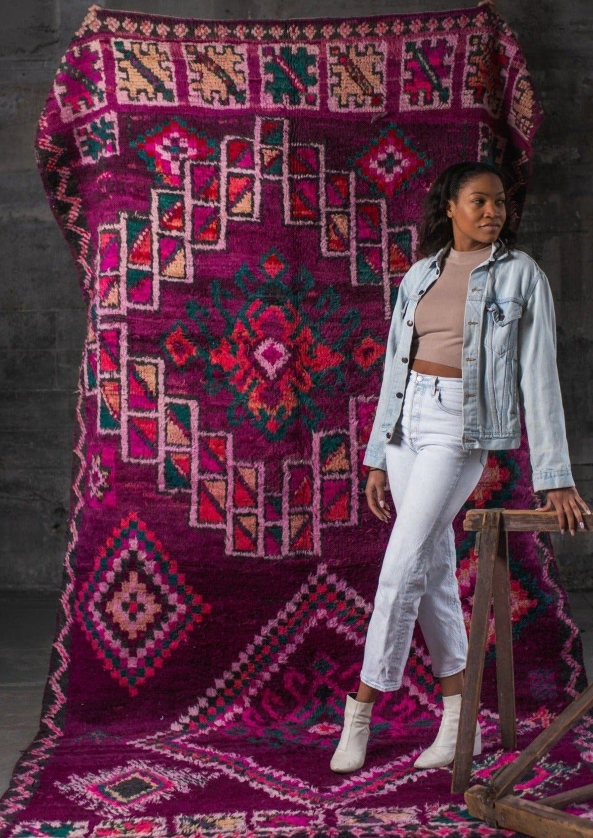 black women empowering female weavers wearing jean jacket and jean combo next to bright colorful rug maroon green orange and pinks on berber symbols in portland oregon