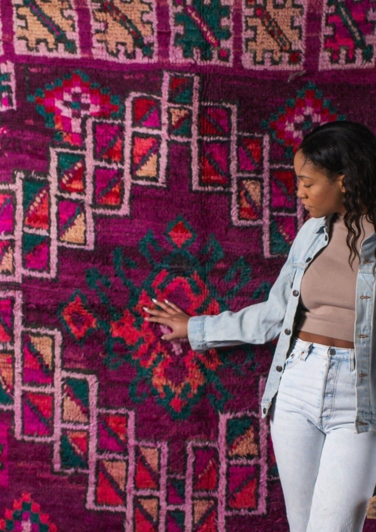 hand touching beautifully designed moroccan rug with berber symbols of protection. beautiful black women wearing Canadian tuxedo, long nails and neutral top fall fashion