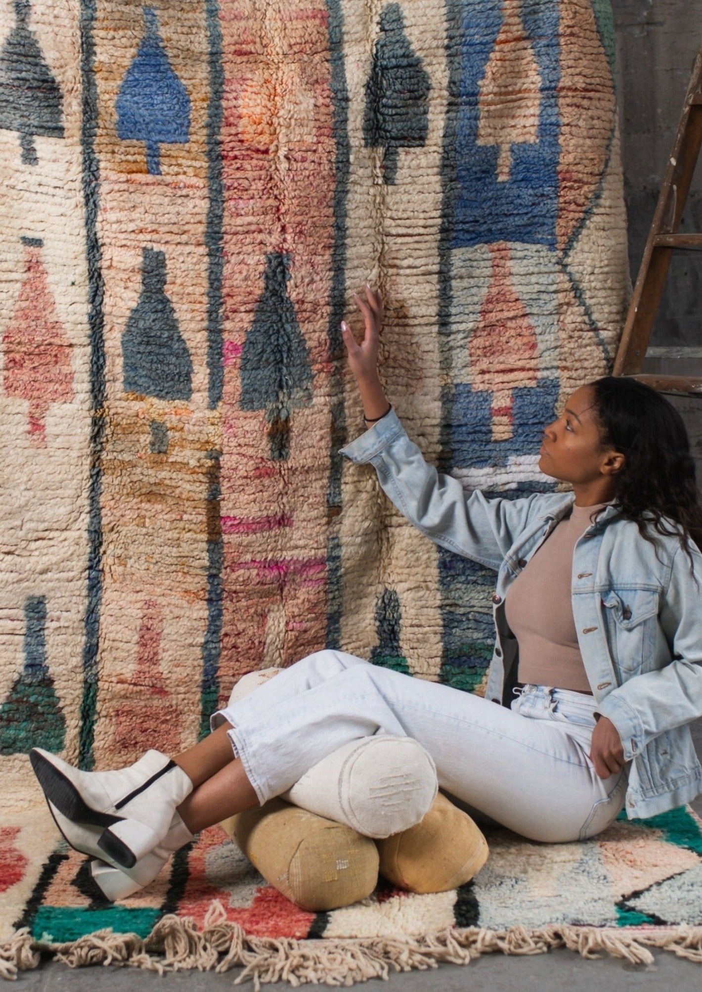 african american girl using three cactus silk lumbar pillows to kick back and relax while admiring a traditional moroccan rug. rustic latter behind her wearing light colored jean outfit. 