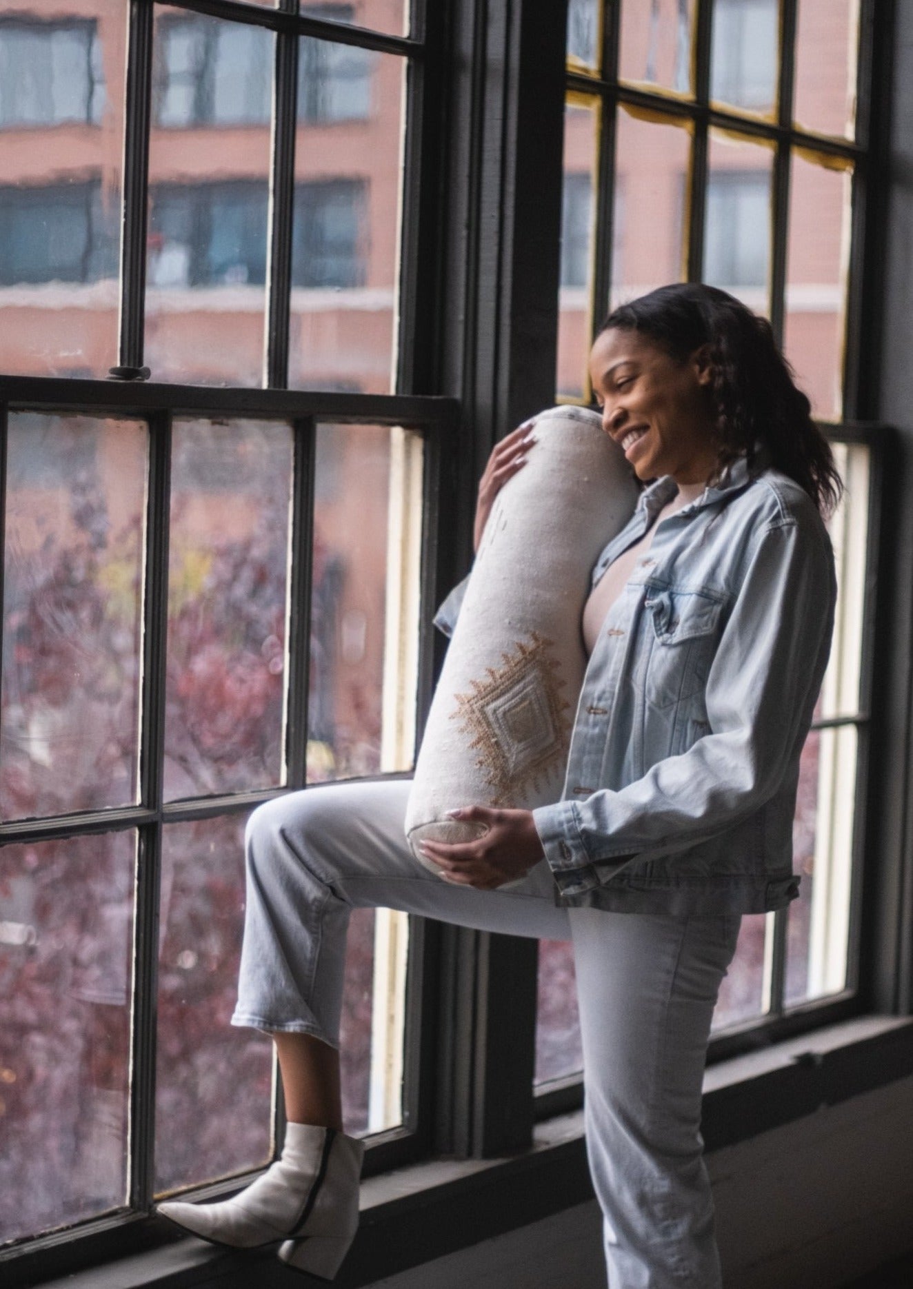 African American girl happily looks out of her loft apartment window after receiving her favorite gift of the season a white pillow made in morocco by female berber women 