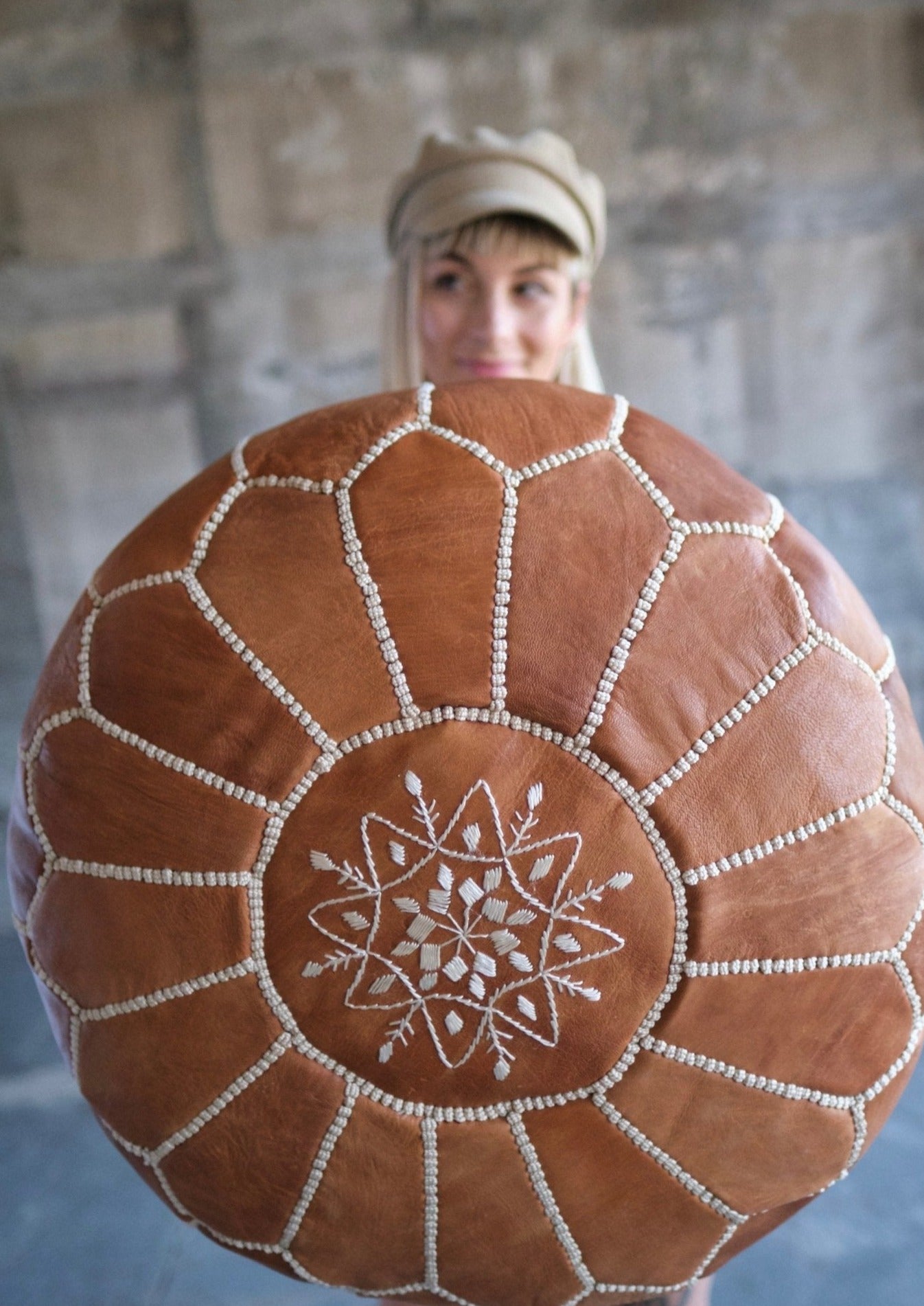 blond girl with cute tan hat holds out pouf to show off the hand stitched motifs on leather 