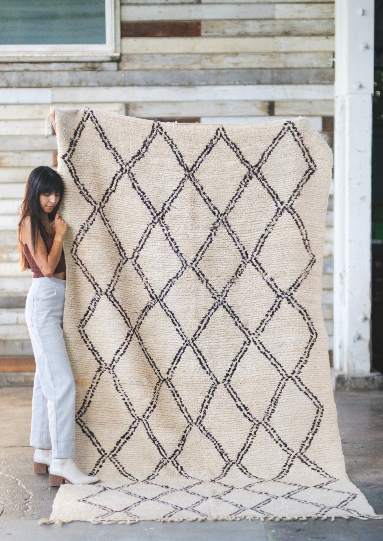 girl holds classic beni ourain rug close, lovingly adores it and is cozy soft standing in rustic scene