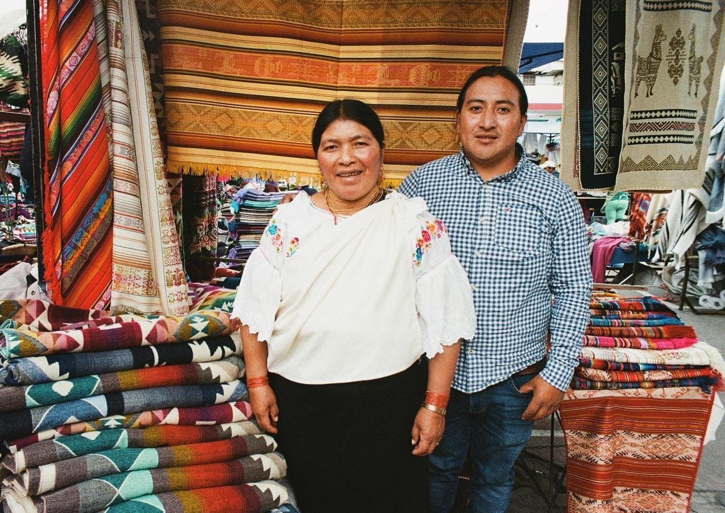 Artisans of Ecuador captured on film. They stand outside at their market displaying the handmade textiles. 